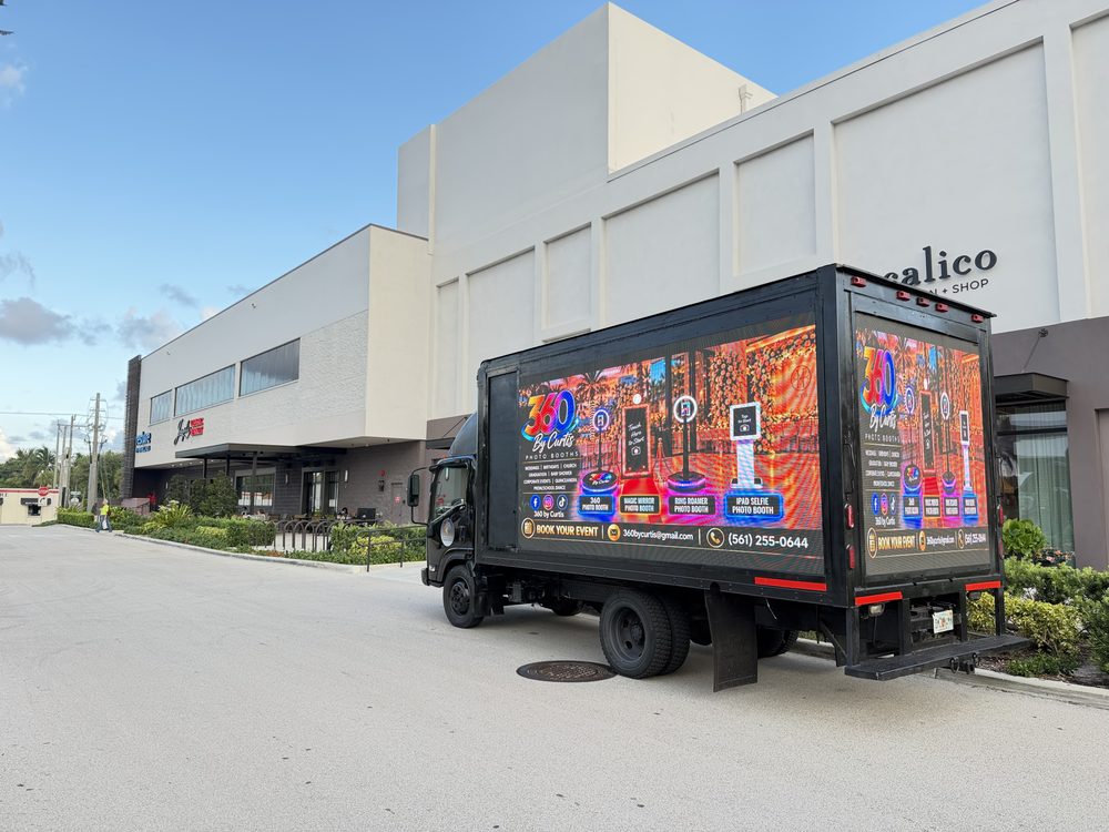 Black box truck with lit LED screens on the passenger side and rear, parked outside a building